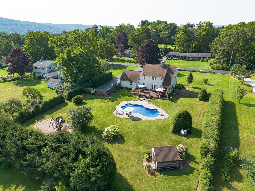 Aerial view of a suburban home with a large in-ground pool and beautifully landscaped yard in a green neighborhood.