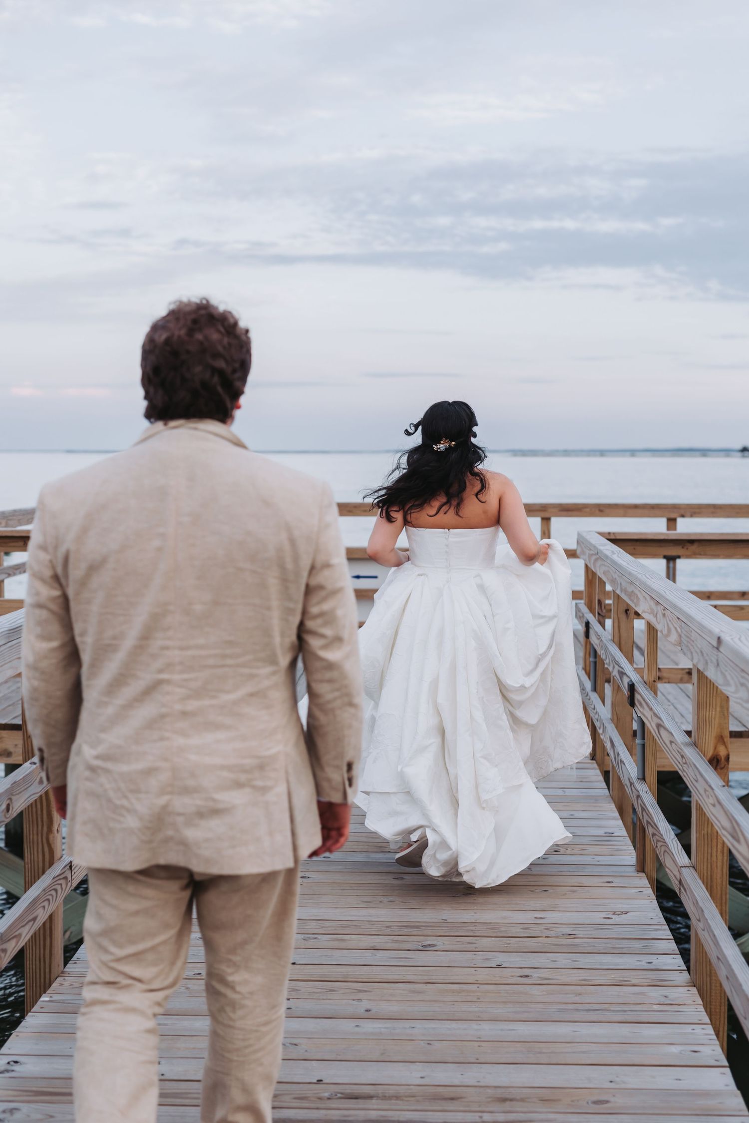 Two brides in white gowns pose elegantly at a bar with warm orange walls and string lights.