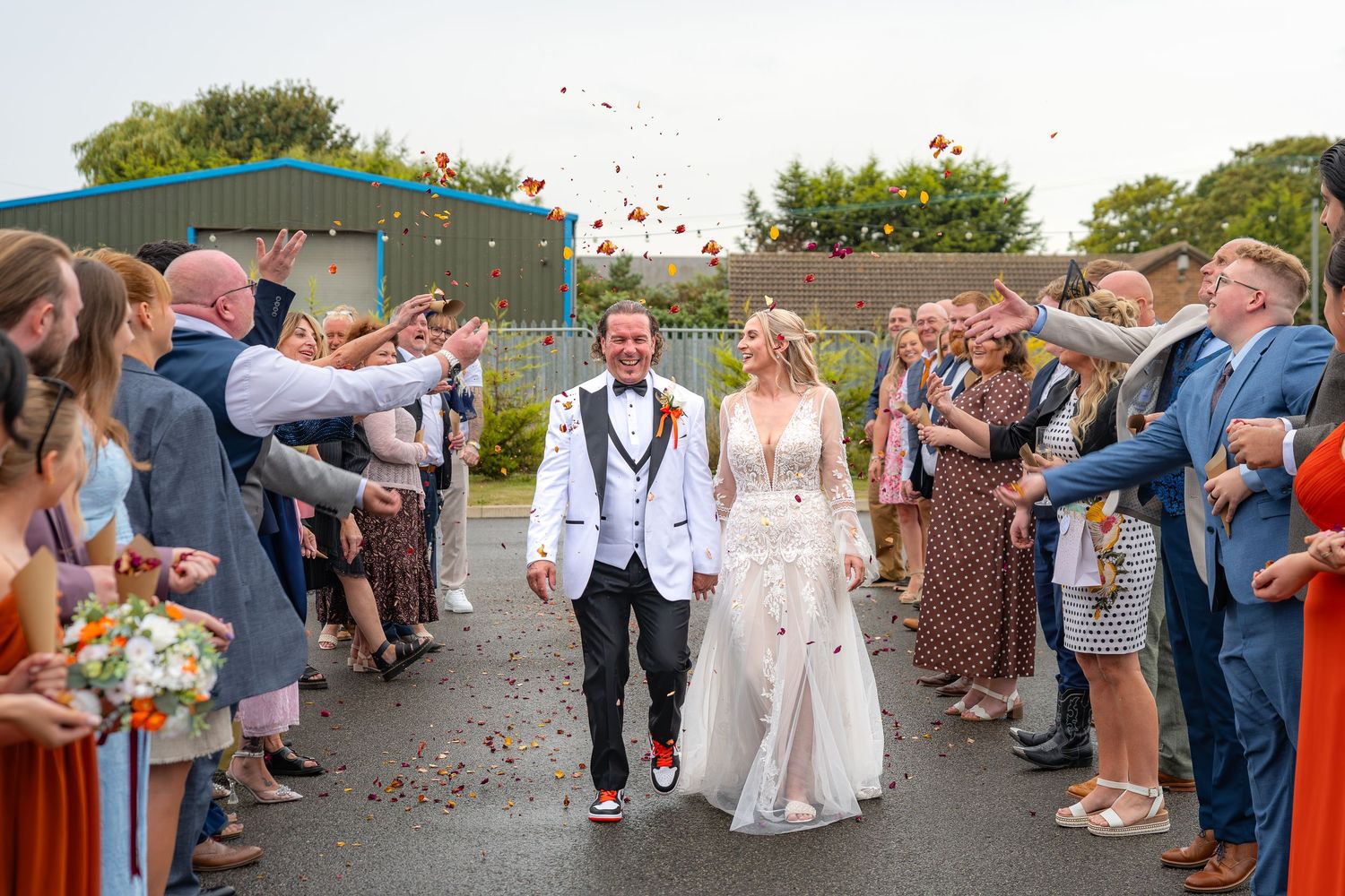 Newlywed couple walks through confetti shower as wedding guests celebrate outdoors on sunny day.Yorkshire, Sheffield, Lincolnshire, UK