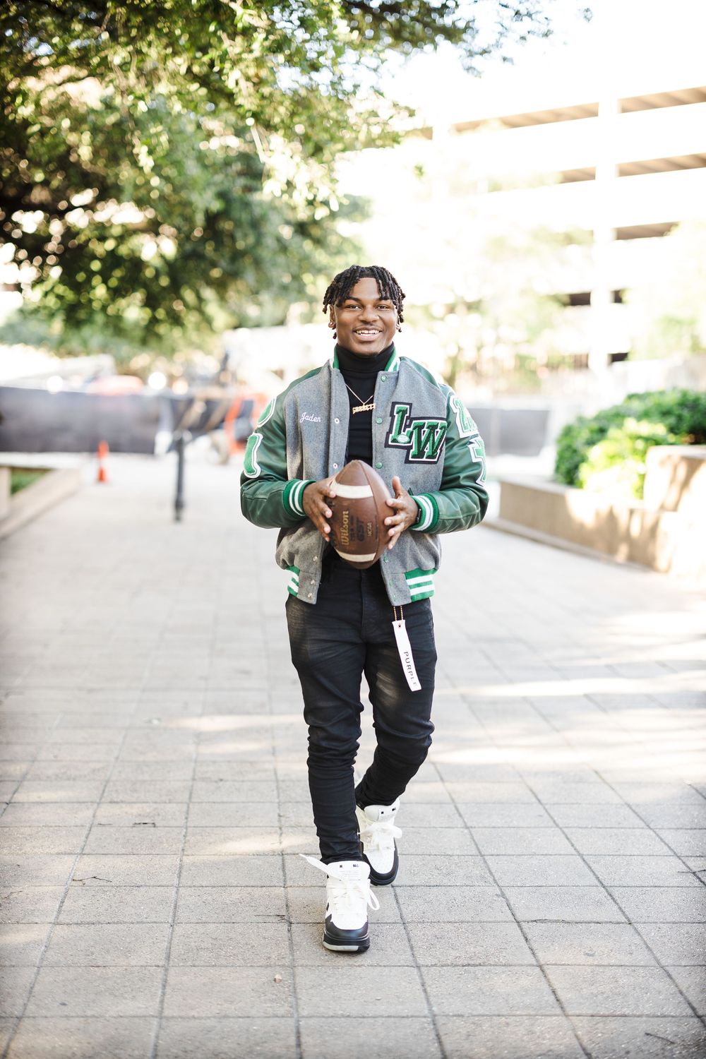 A student in a green letterman jacket and black pants poses in various casual stances on a paved walkway.