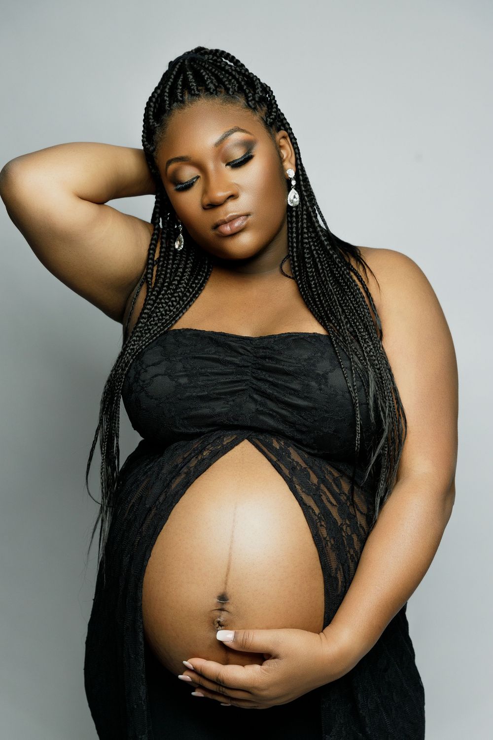 A maternity photoshoot series showing a pregnant person in a black top posing gracefully against a gray backdrop.