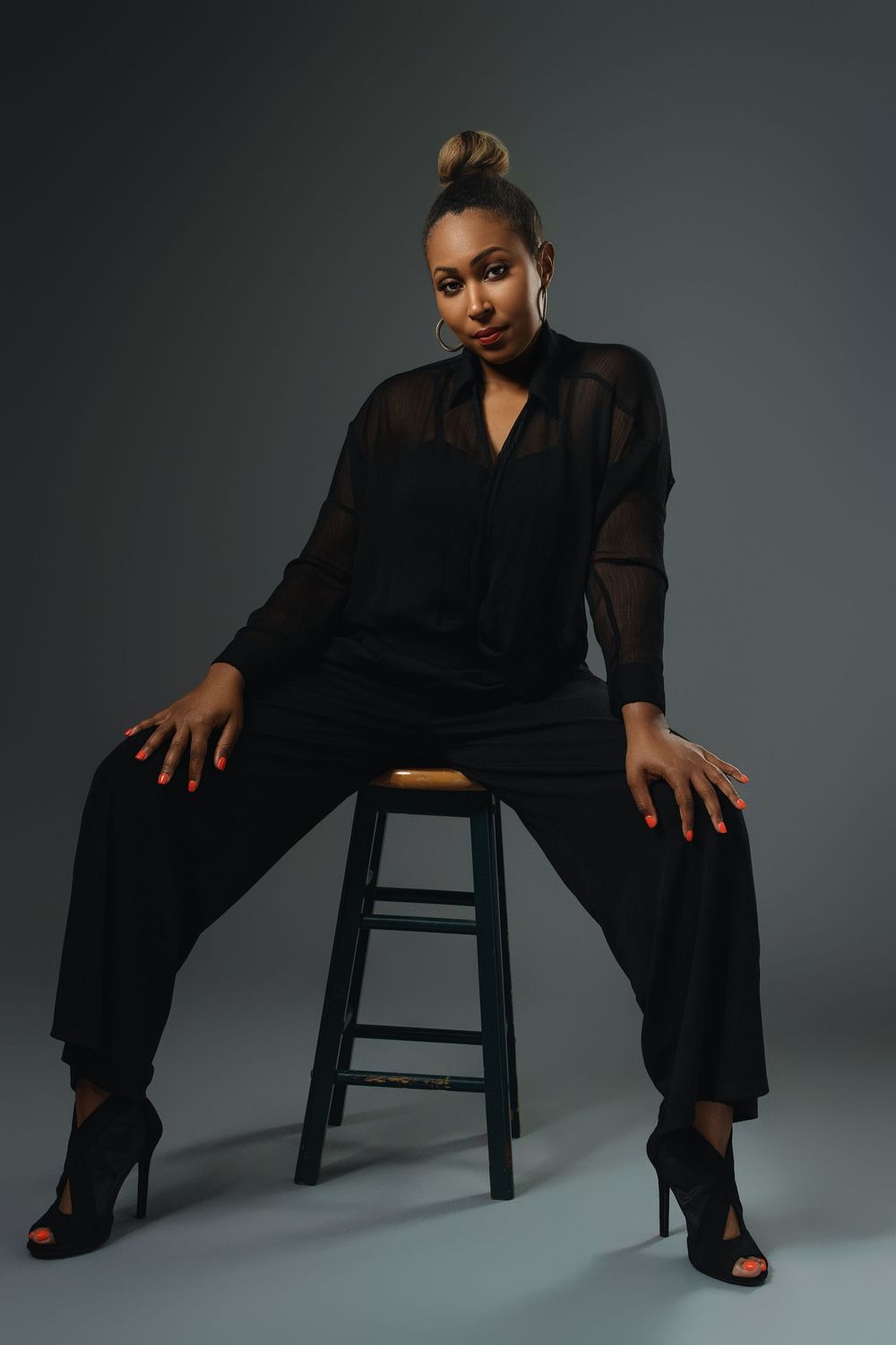 A series of fashion portraits showing a model in a black outfit striking different poses on a dark stool against a gray backdrop.