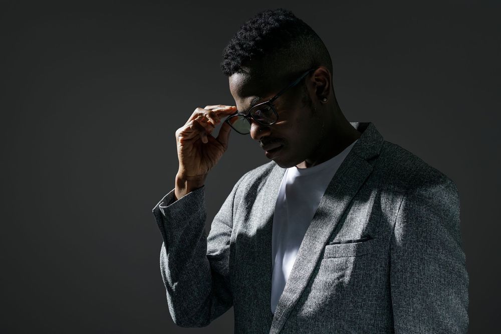 A series of moody black and white portraits showing someone in a suit jacket adjusting their glasses in dramatic lighting.