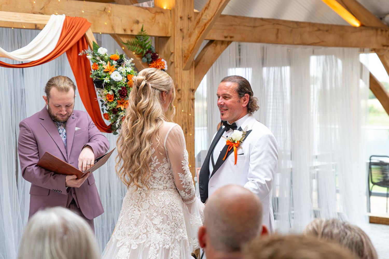 Bride and groom exchange vows at rustic barn wedding ceremony with officiant, orange floral arch decor.Yorkshire, Sheffield, Lincolnshire,
