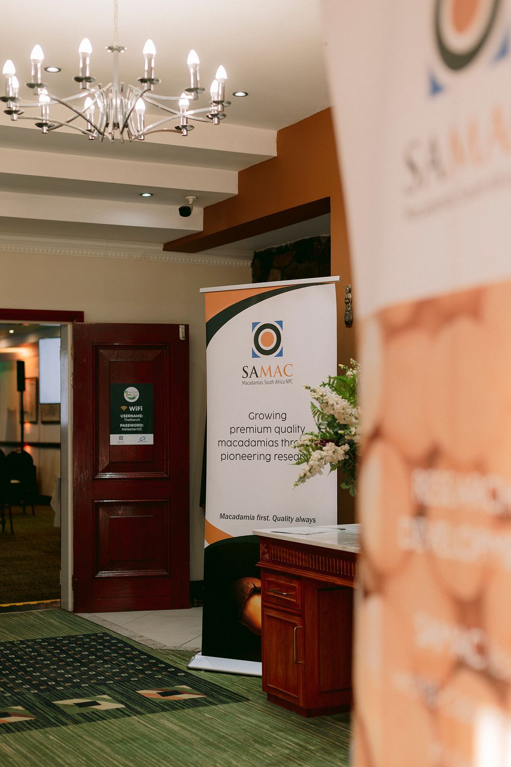 SAMAC macadamia industry banner display in hotel conference venue with chandelier lighting and wooden doors.