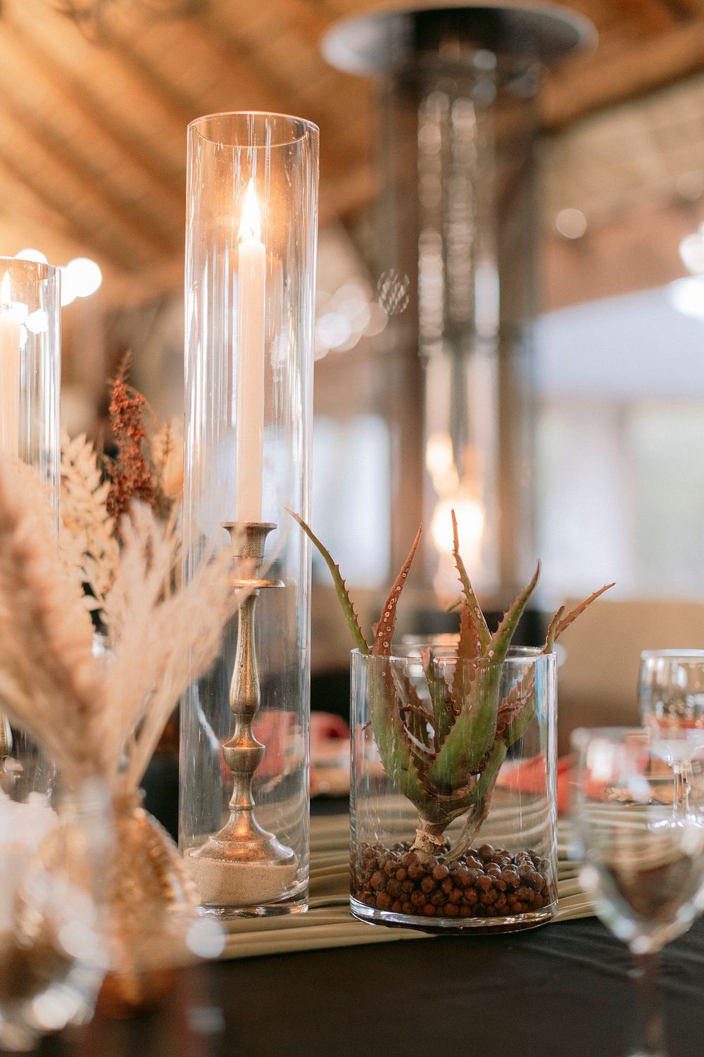Elegant table centerpiece with tall glass candle holders, succulents in glass vases, and dried pampas grass decor.