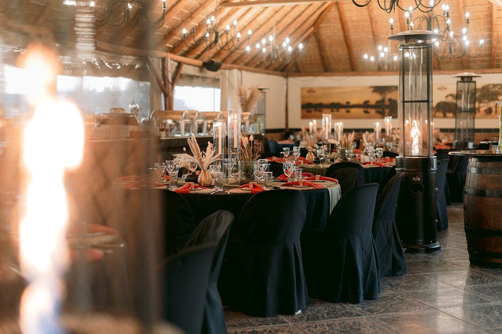 Elegant wedding reception venue with black draped tables, candles, and warm string lights in a rustic barn setting.