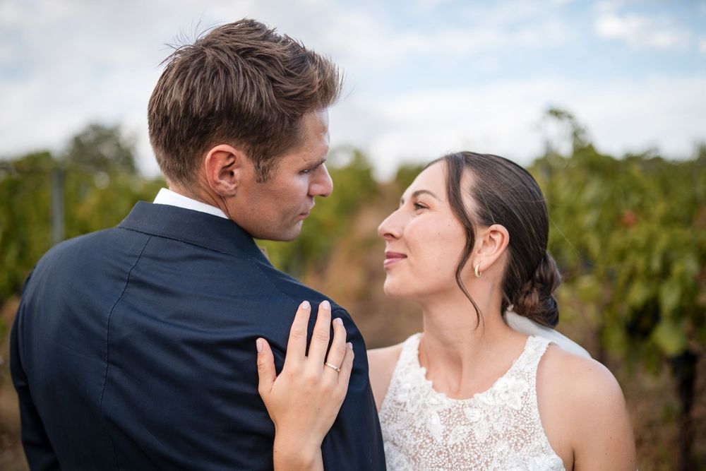 Bride and groom share a romantic moment in a vineyard, with the bride smiling up at her partner in wedding attire.