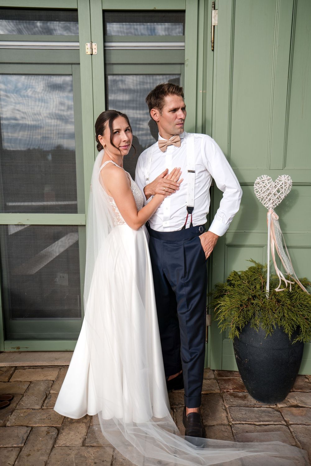Bride in white gown and groom in navy suit with bow tie pose together outside green doors on their wedding day.