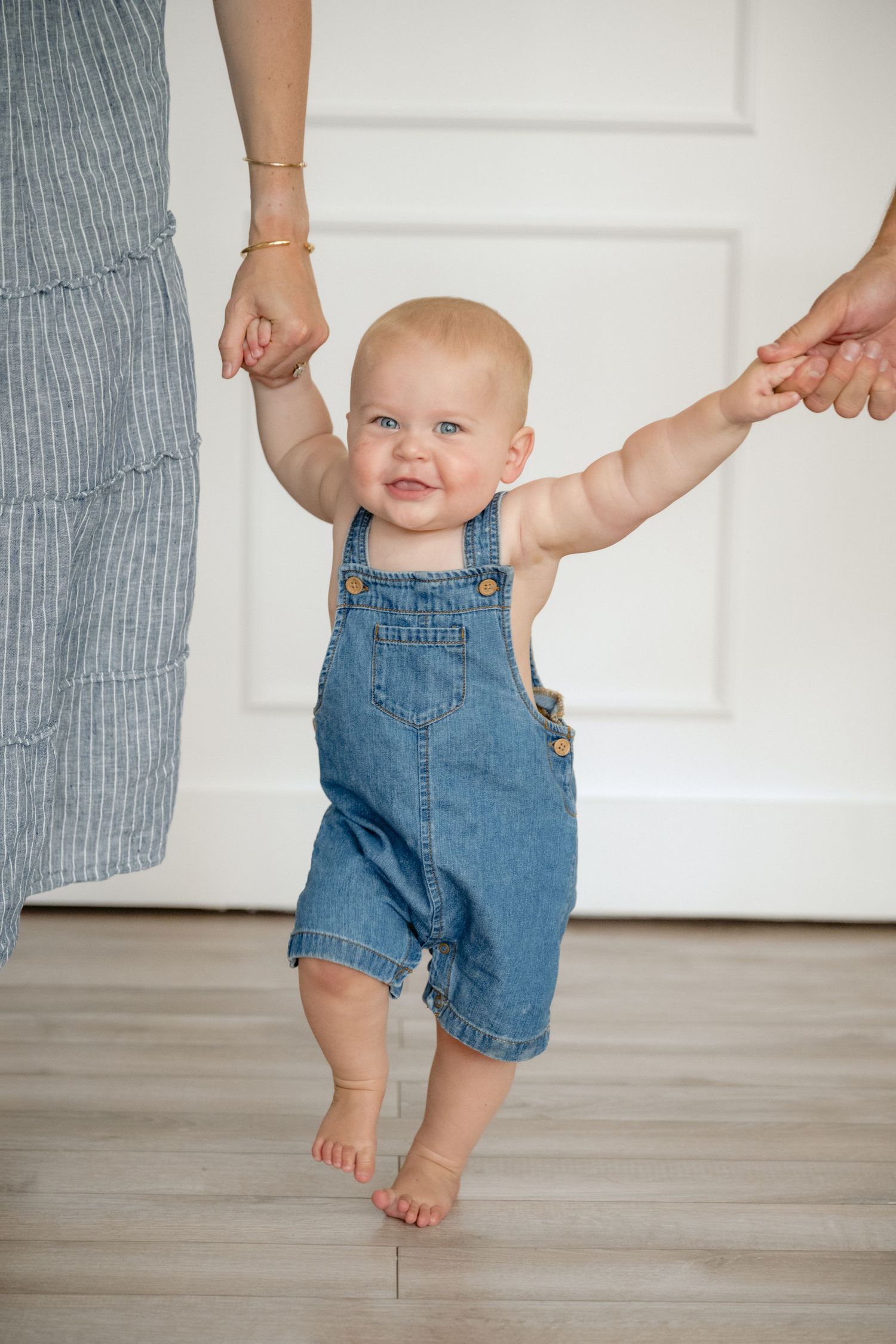 Parents hold baby boys hand as he learns to walk during an in-studio one year milestone session in New Richmond, WI.