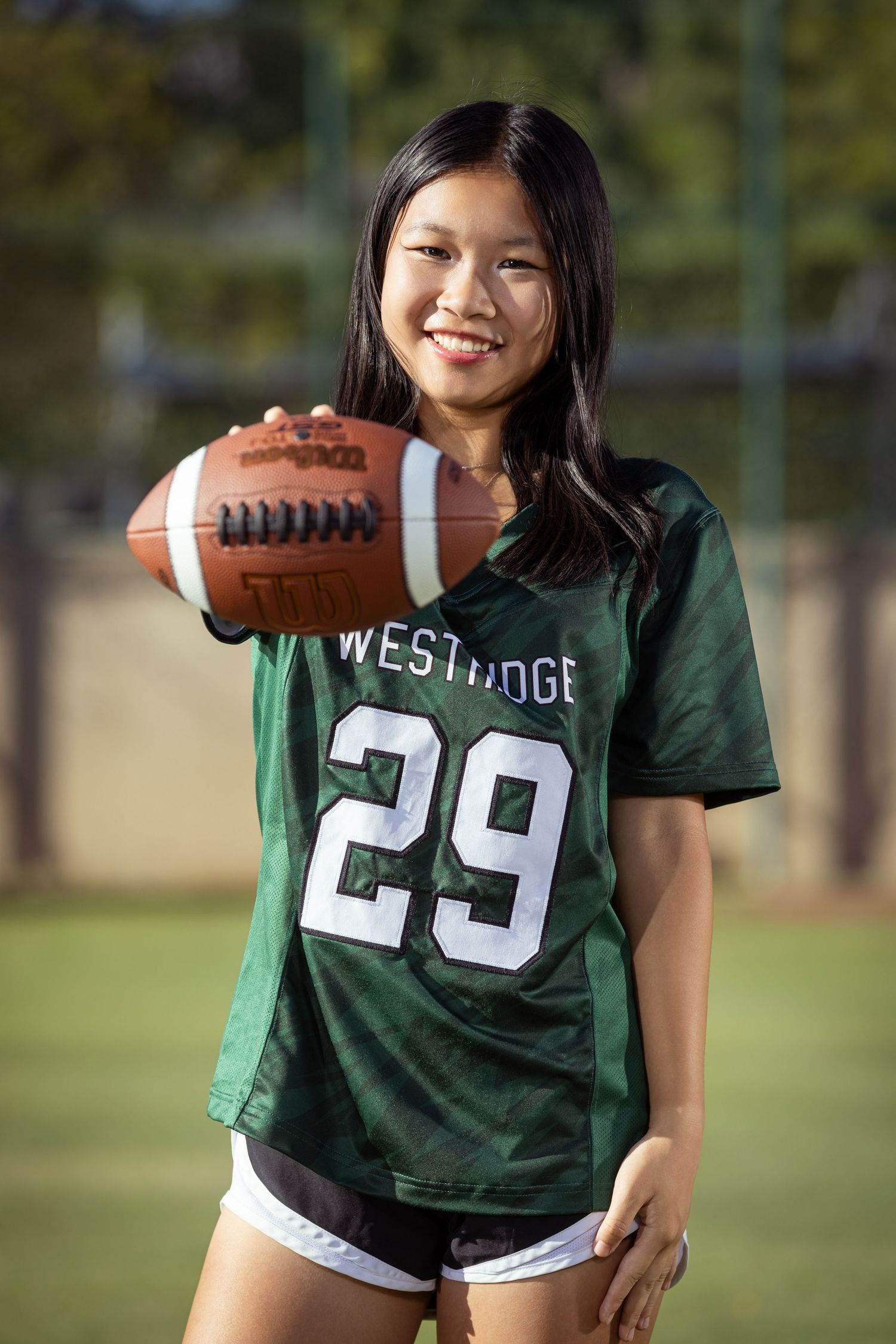 Young woman in Westridge #29 green football jersey smiling and holding a football on a sports field.