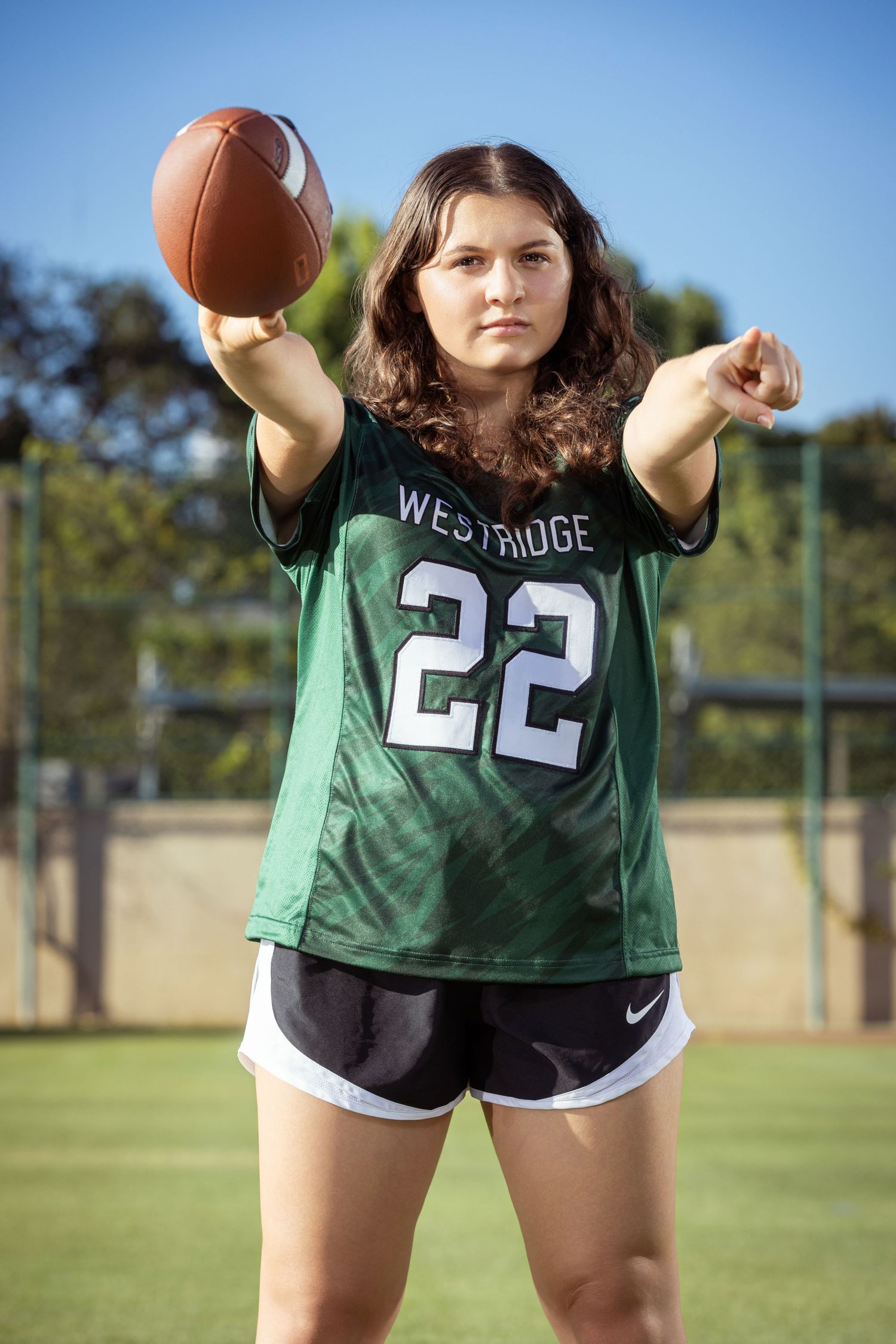 Young woman in Westridge #22 green football jersey poses with football on outdoor field.