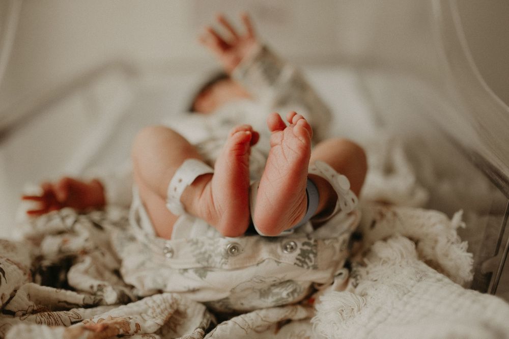 Newborn baby lying on a soft blanket with tiny bare feet raised toward the camera in a cozy, natural-light setting.