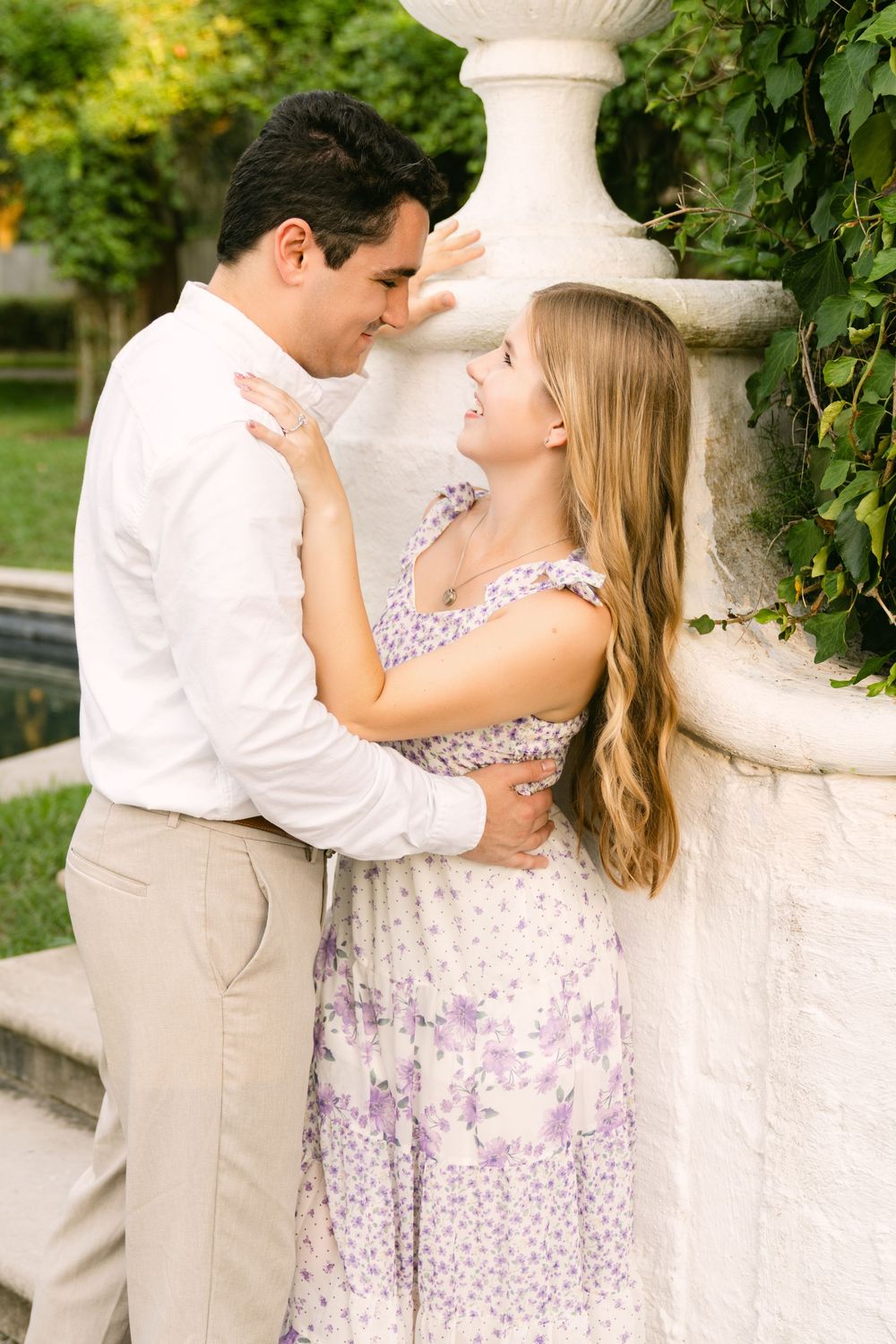 Engaged couple embracing beside an ivy-covered white garden wall during their Jekyll Island engagement portrait session.