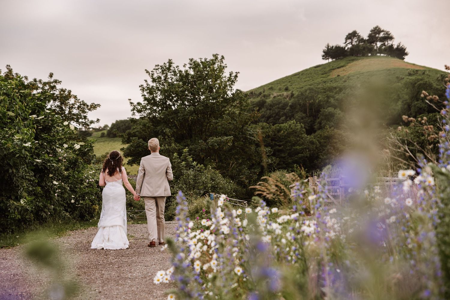 Black and white photo of a bride and groom walking hand in hand through a lush forest path on their wedding day.