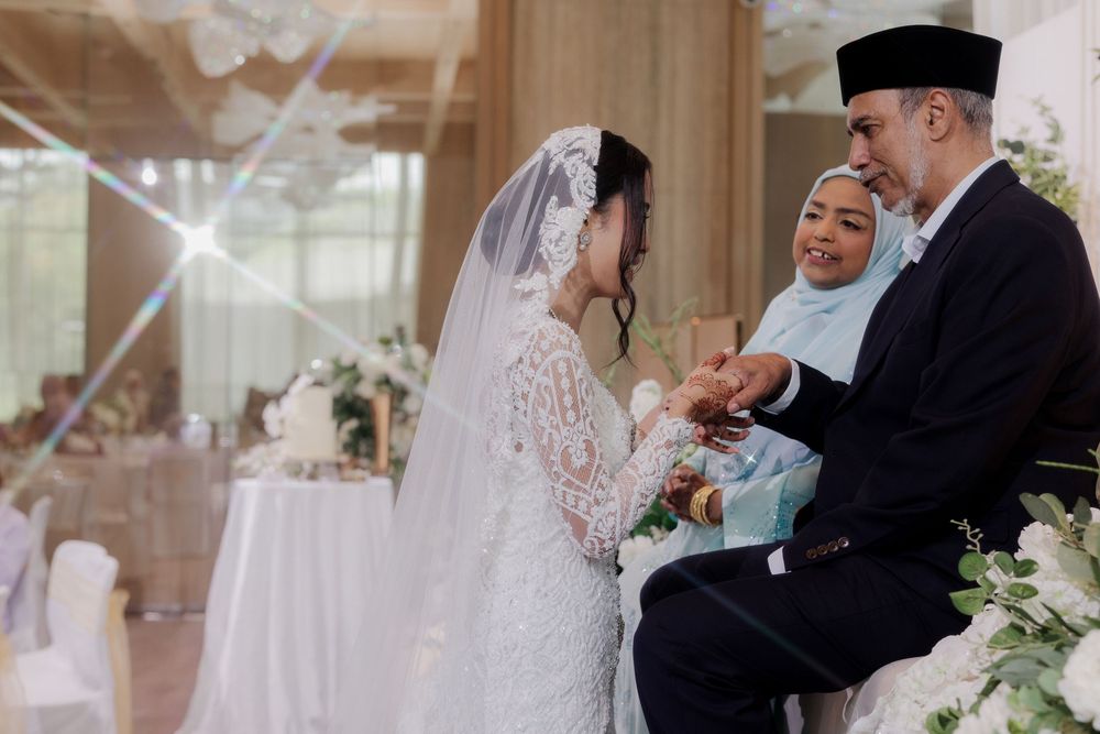A bride in white lace gown and veil exchanges rings with an older man at an elegant Muslim wedding ceremony.