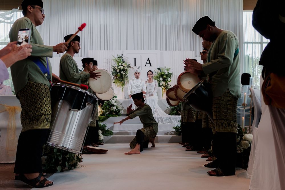 Traditional Malay wedding ceremony with kompang drummers performing in a decorated hall with floral backdrop.