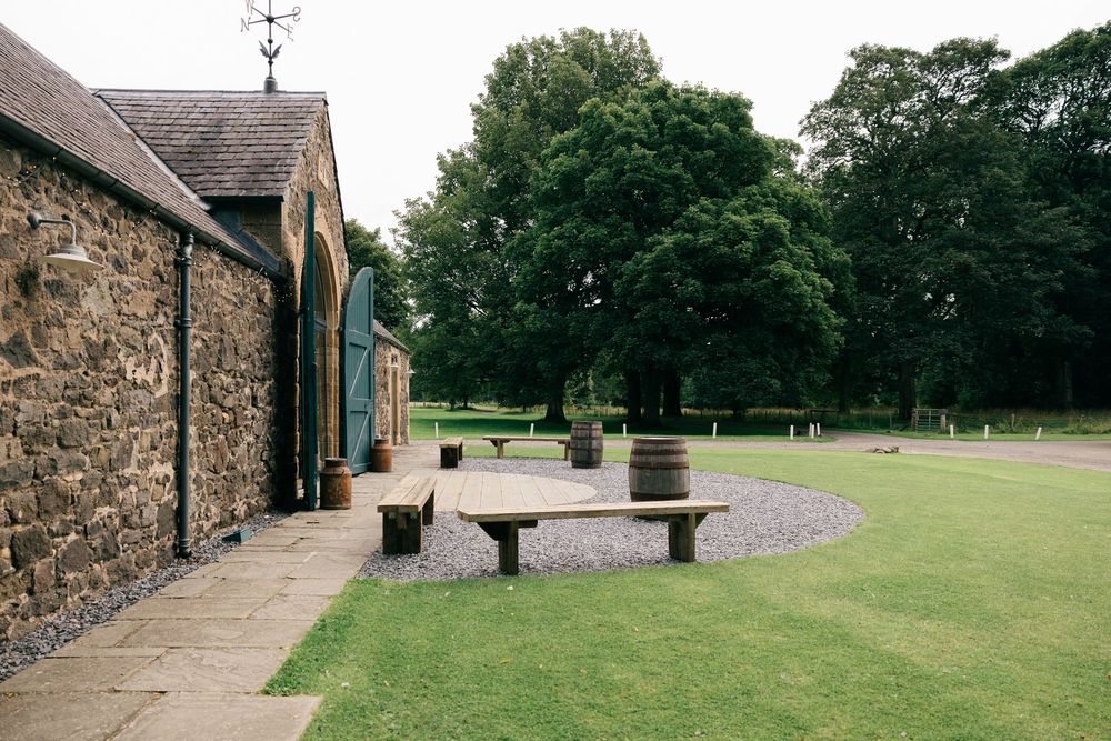 Stone barn venue with wooden barrels and benches on manicured lawn.