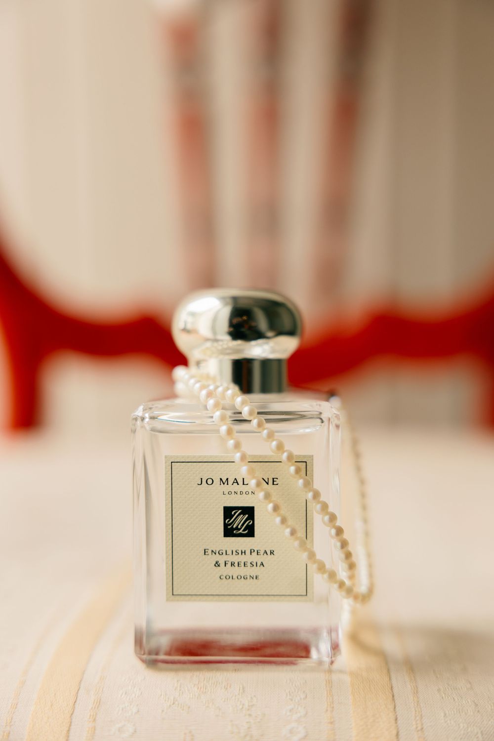 Jo Malone English Pear and Freesia cologne bottle with pearl necklace on wedding day flat lay.