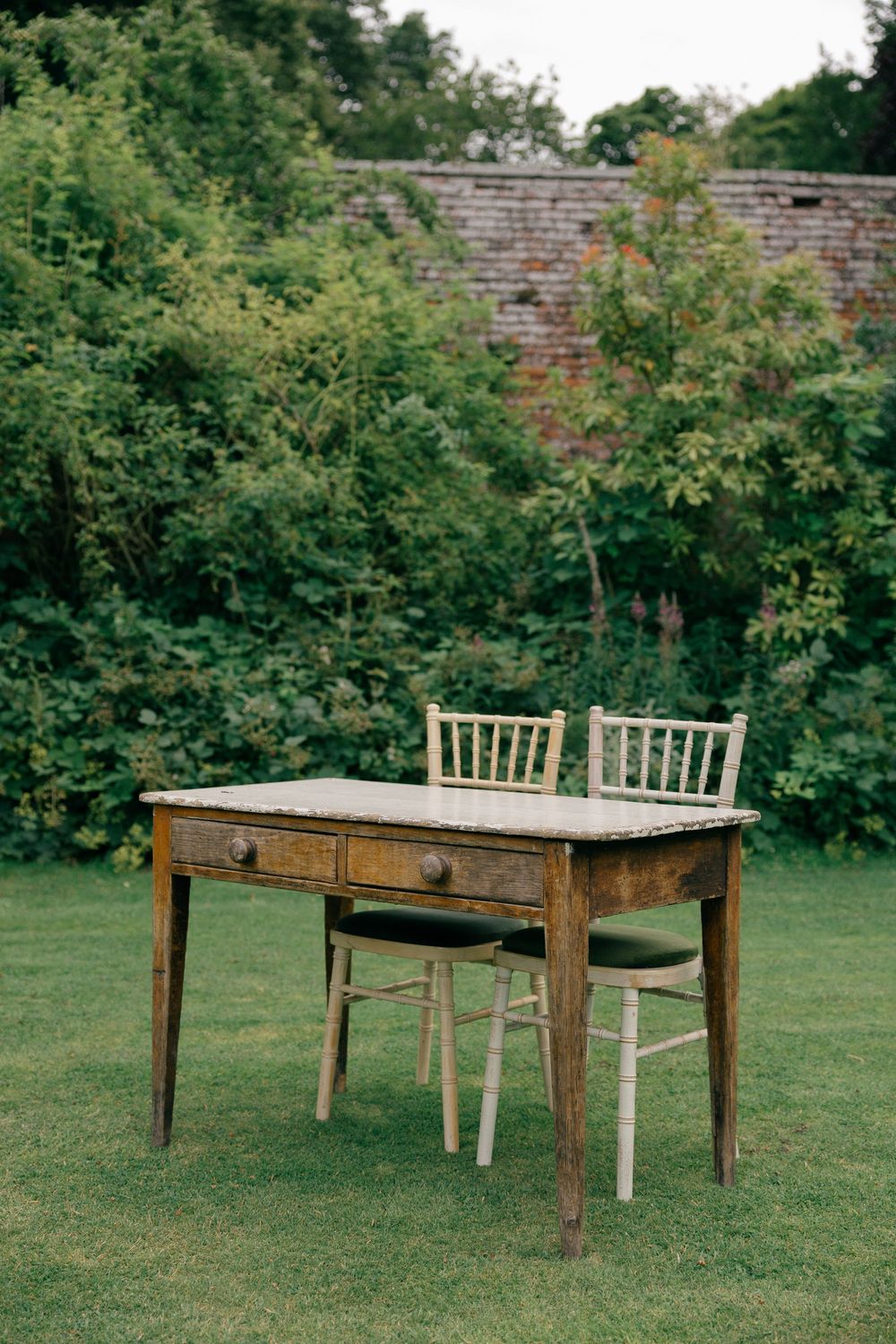 Rustic wooden desk with two chairs on green lawn in garden setting.