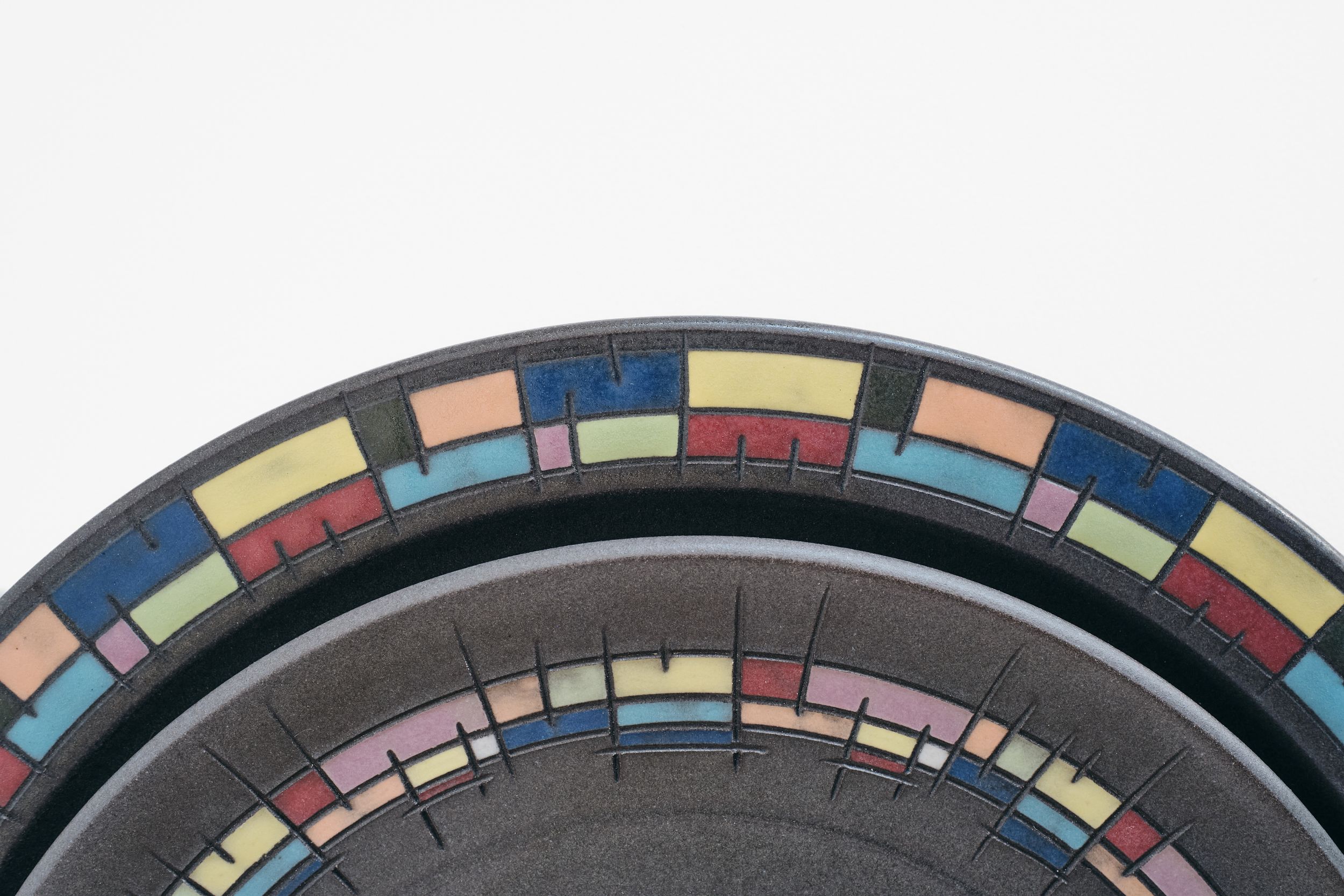 Close-up of stacked black ceramic plates with colorful mosaic-style rims in blue, yellow, red, green, and pink rectangular tiles.