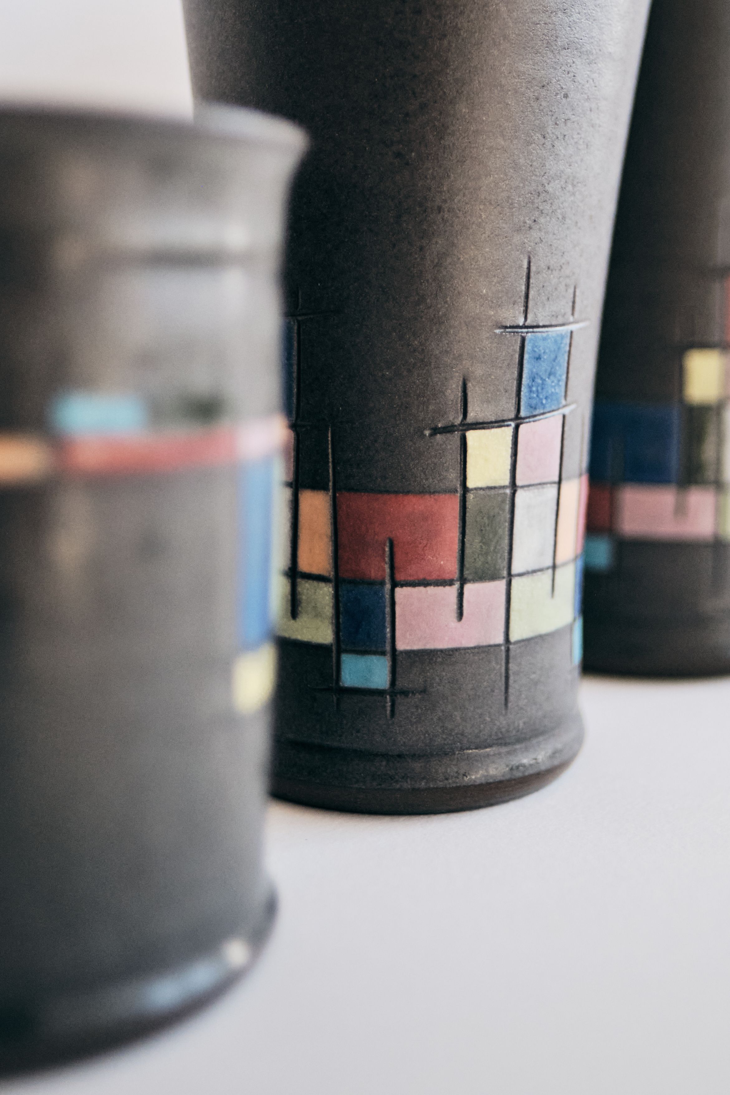 Handmade dark gray ceramic vases with a Mondrian-inspired grid pattern of pastel pink, blue, yellow and green color blocks.