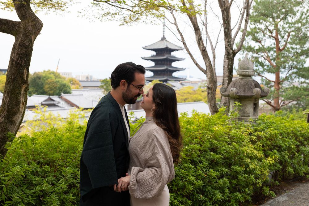 Couple in traditional Japanese attire sharing a kiss in a garden with a stone lantern and a historic pagoda in the background.