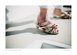 Close-up of a person's feet in decorative gold sandals with colorful beads, standing on a sunlit boat deck casting soft shadows.