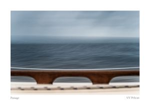 Wooden boat railing frames the calm gray ocean and hazy horizon in a moody passage photograph aboard SV Pelican.