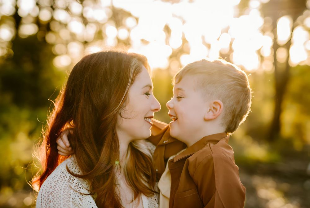 A mother and young boy share a sweet nose-to-nose moment outdoors in golden sunset light.