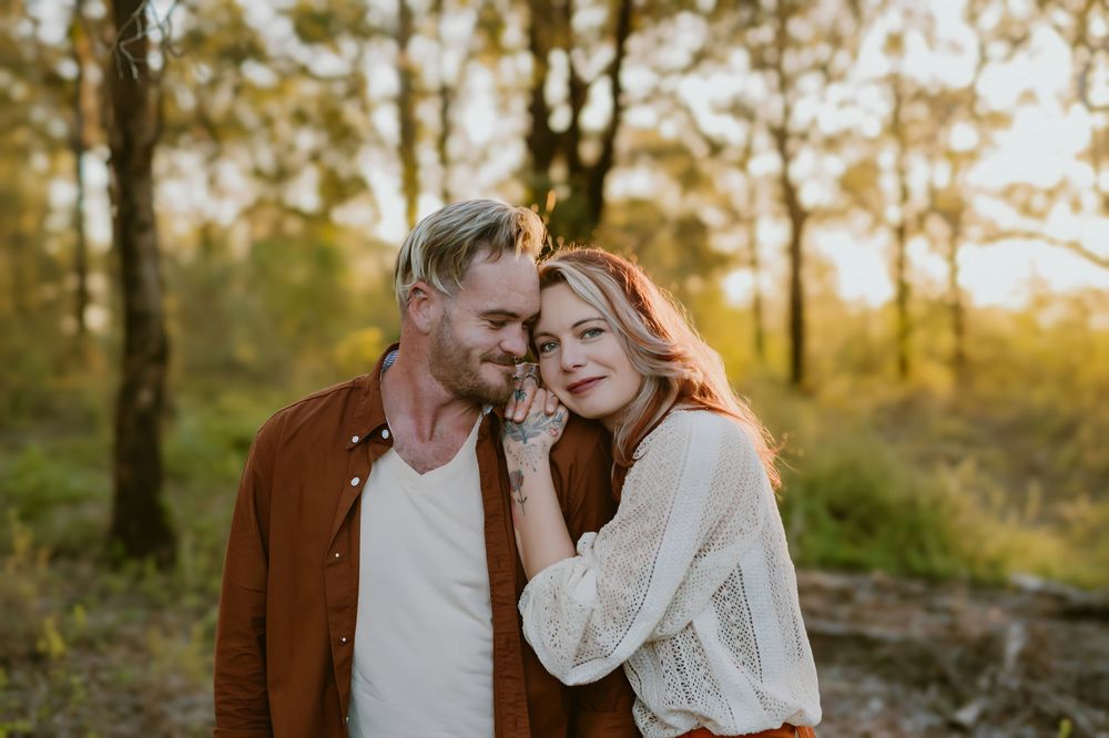 A couple shares a tender romantic moment outdoors in a sun-dappled forest during golden hour.