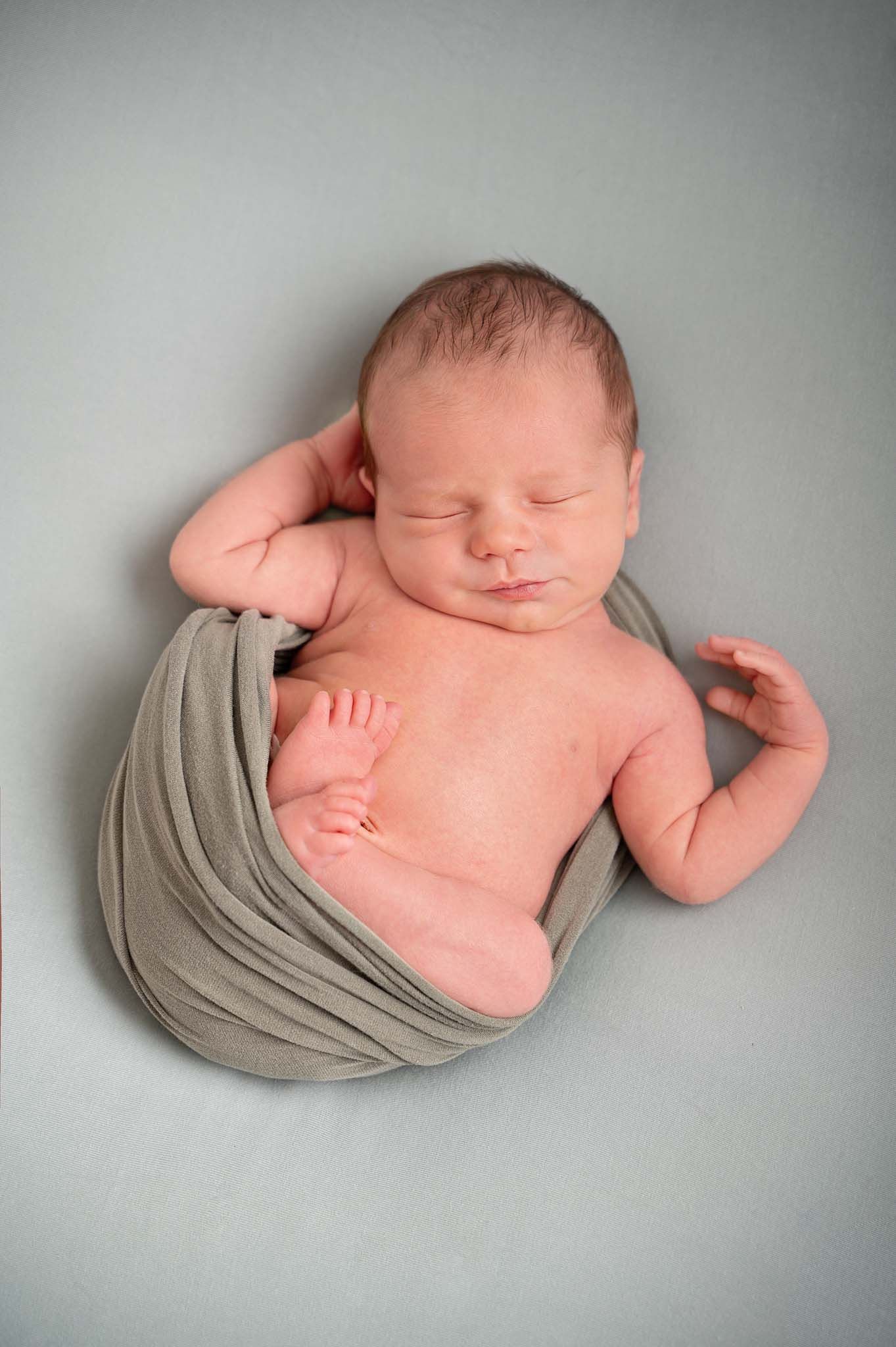 Newborn baby posed naturally on his back wrapped in sage green blanket in studio session in Baltimore, Ontario