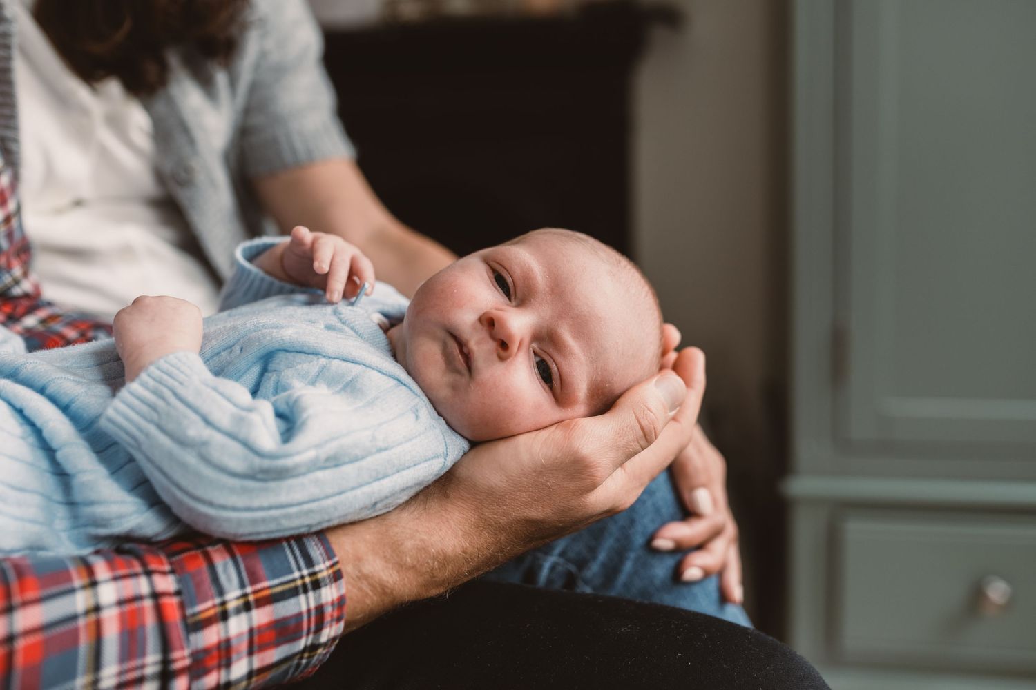 A newborn baby resting peacefully in a parent's arms, dressed in a soft blue onesie.