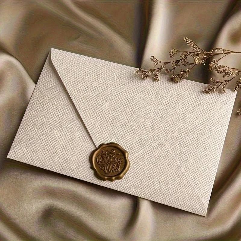Elegant ivory envelope with gold wax seal on silk fabric, accented by dried flowers, perfect for luxury wedding invitations.