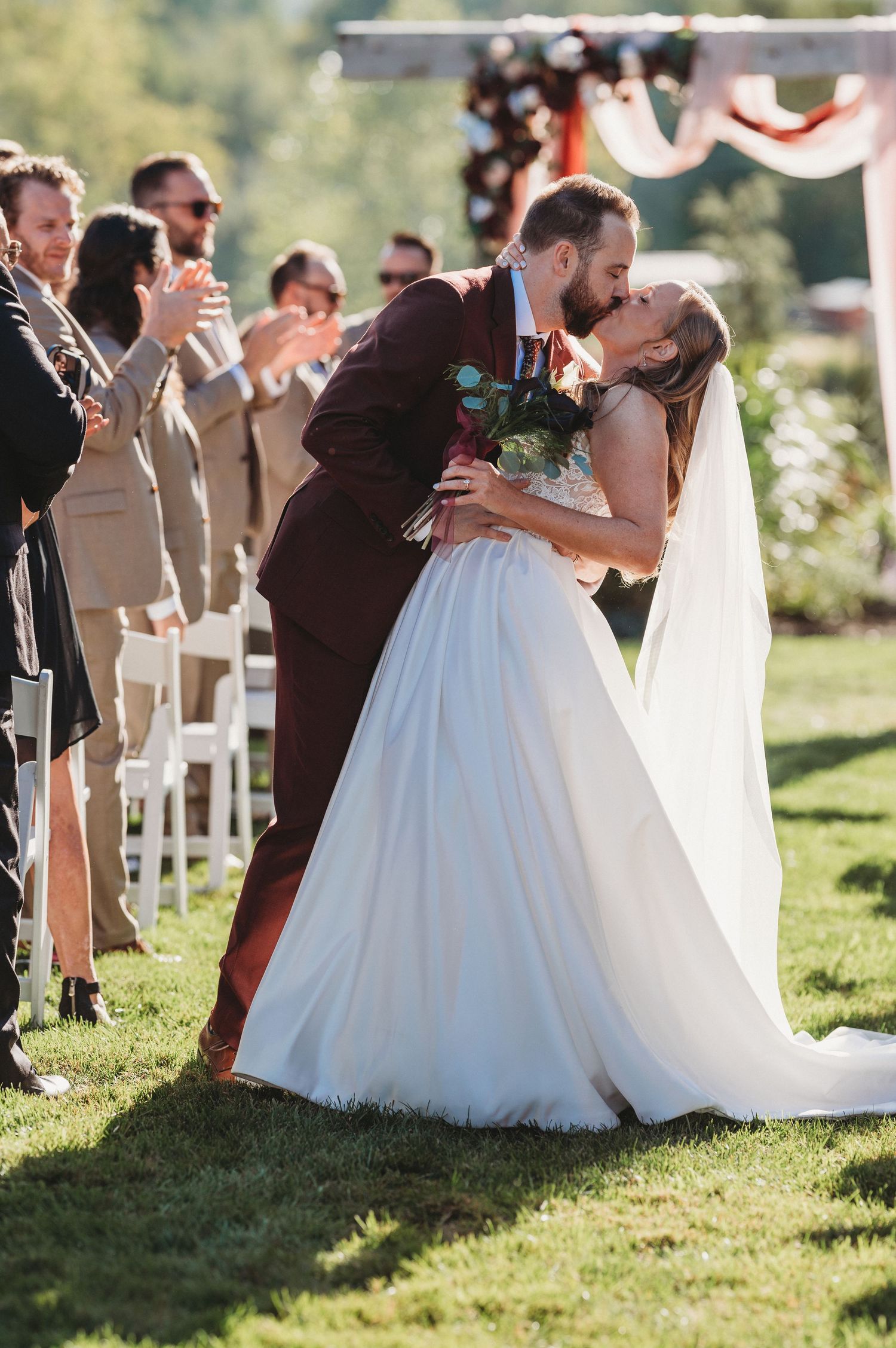 Groom dipping and kissing the bride in the aisle as wedding guests applaud.
