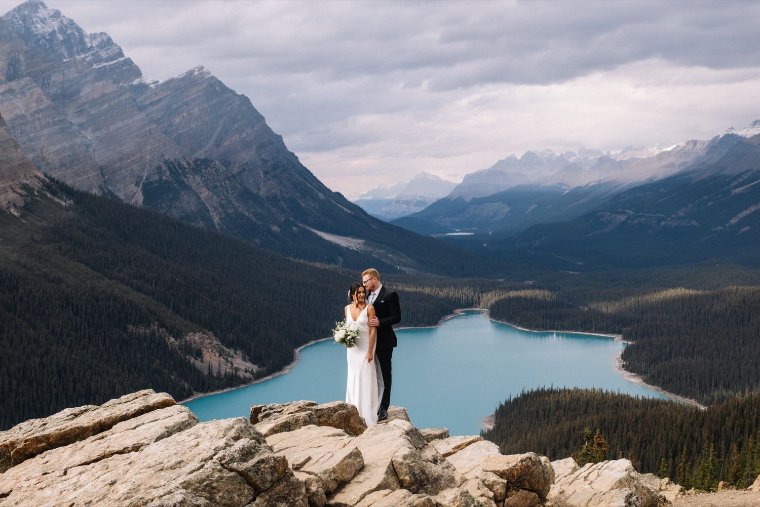 Calgary wedding photographer – bride and groom embracing above a turquoise mountain lake near Banff