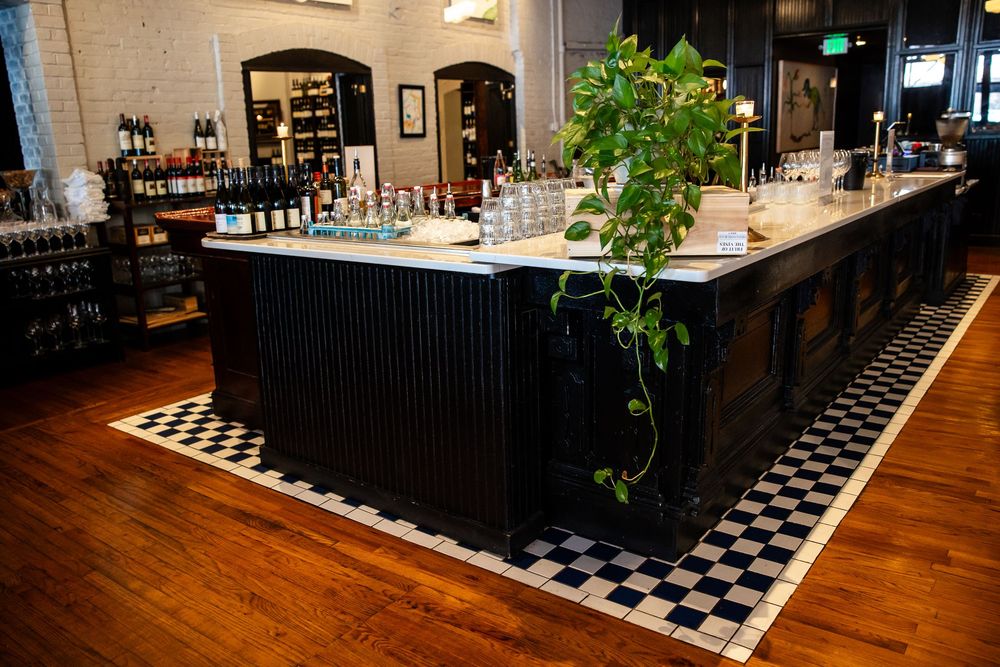 Elegant black bar with checkered floor, glassware, and green ivy plant centerpiece in an upscale restaurant interior.