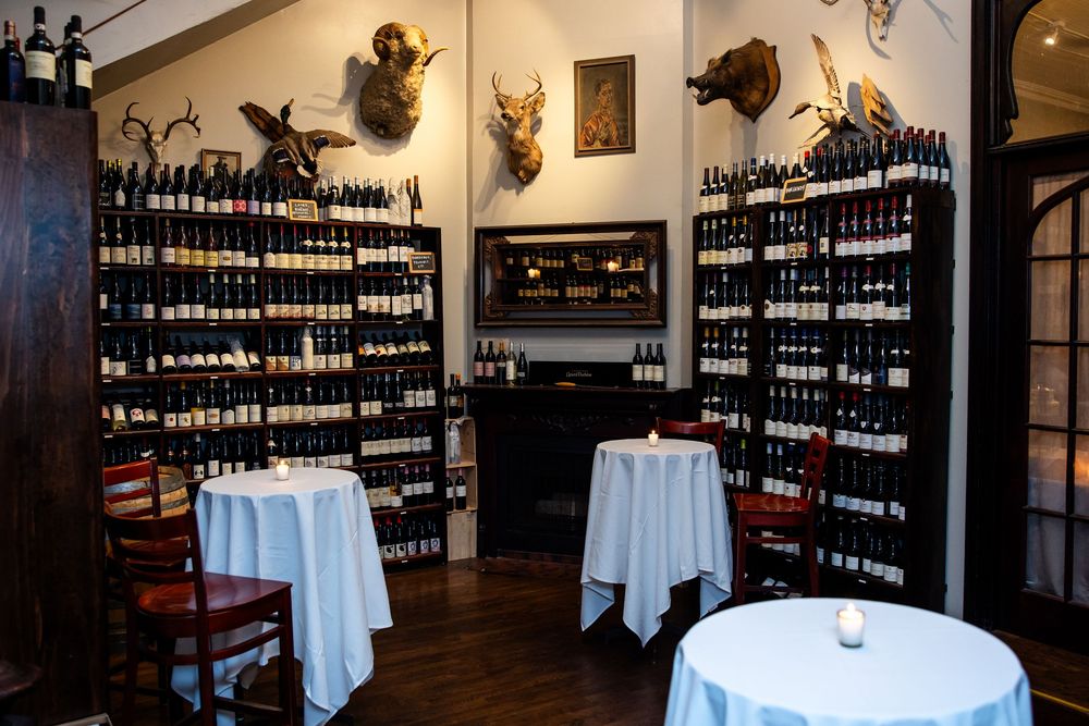 Cozy wine bar dining room with floor-to-ceiling wine racks, white tablecloths, and mounted animal heads on the wall.