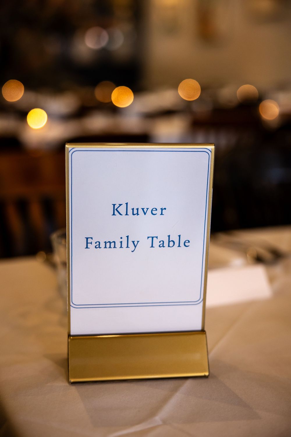 Gold table card holder displaying Kluver Family Table sign at an elegant wedding reception dinner.