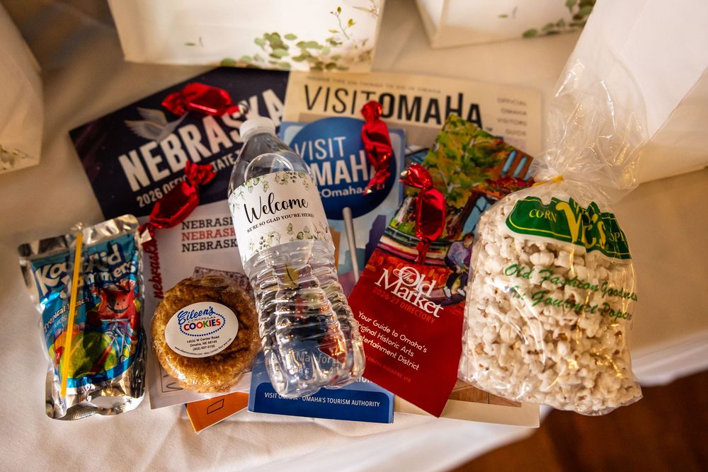 A Welcome gift basket featuring Nebraska and Visit Omaha souvenirs, popcorn, snacks, and a water bottle on a white surface.