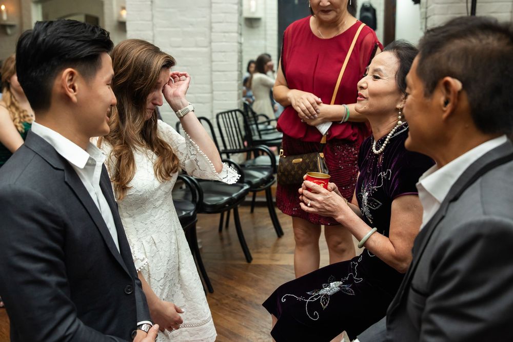 Guests laughing and socializing at an elegant indoor party, with women in red and black dresses conversing with a couple.