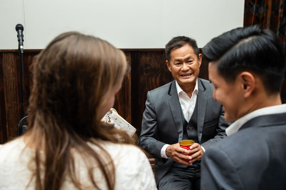 Man in gray suit smiling and holding a drink while conversing with two guests at a formal event.