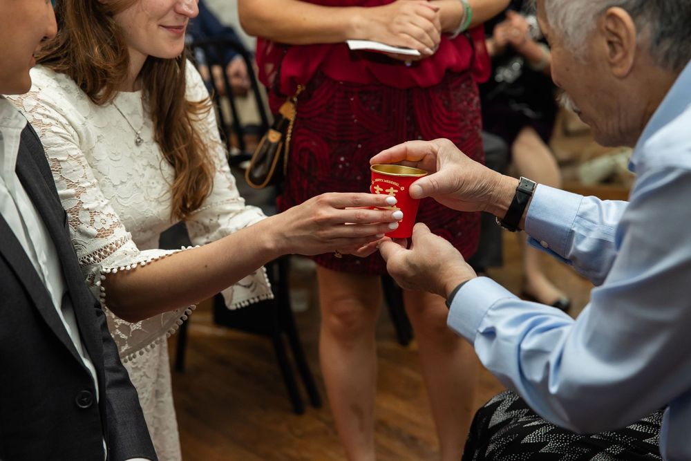 An elderly man presents a red gift box to a young woman in a white dress at a formal gathering.