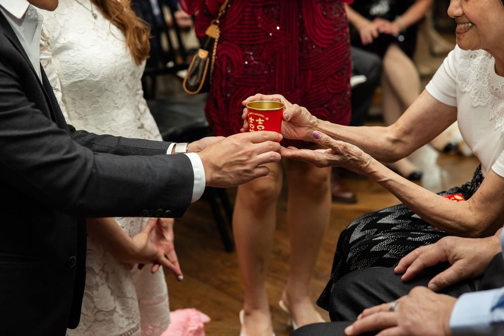 Bride and groom performing a traditional Chinese tea ceremony, offering a red cup to an elder during their wedding reception.