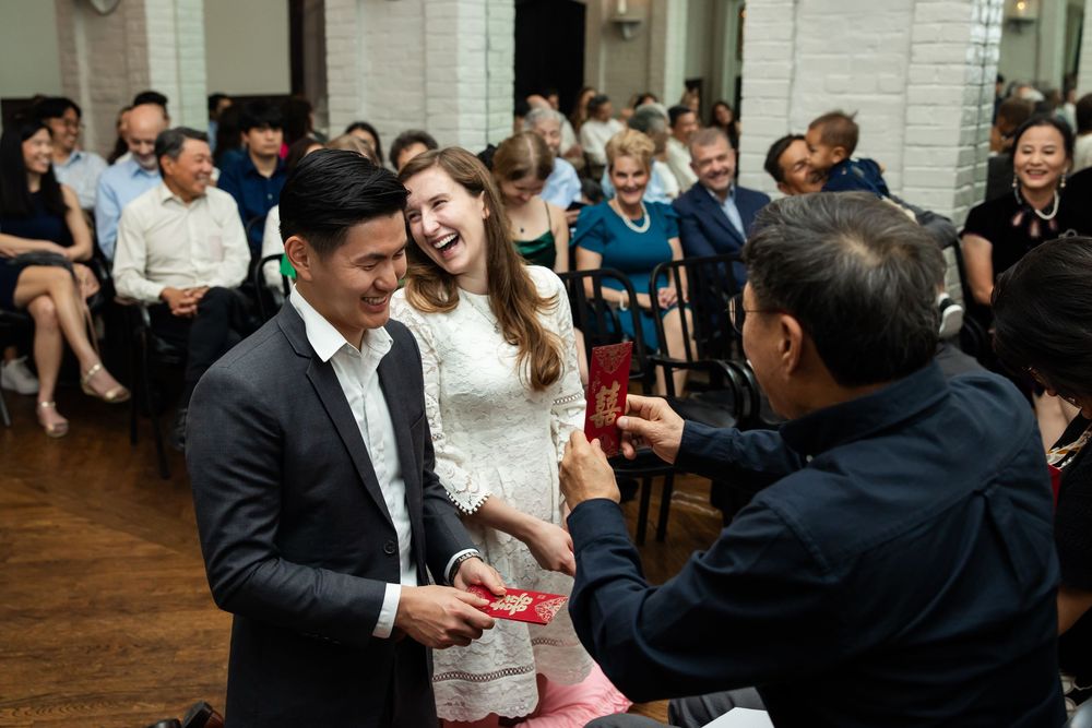 Smiling bride and groom receiving red envelope gift from guest during elegant wedding reception celebration.