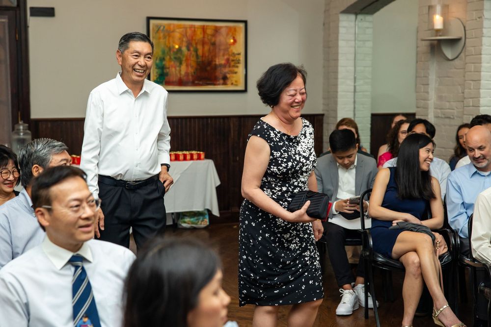 Asian family celebrating at a restaurant gathering, smiling couple standing while guests sit around tables.