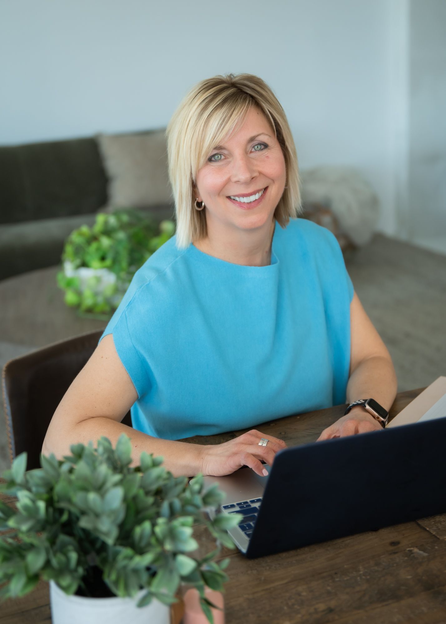 Professional woman in pink blazer reading a business document at a wooden desk with laptop in modern office.