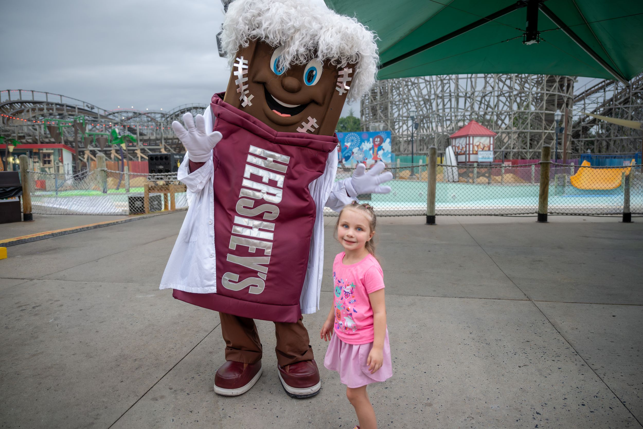 Young girl poses with Hershey's gingerbread man mascot in lab coat at Hersheypark amusement park.