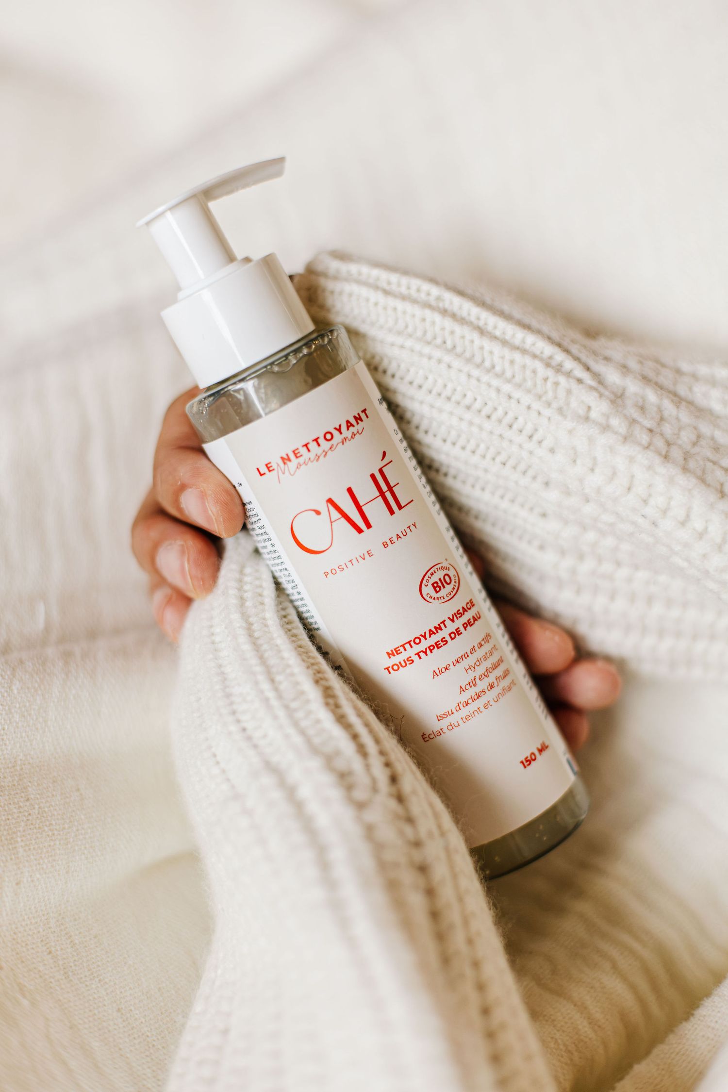 Photographie lifestyle d'un produit cosmétique de la marque française Cahé Cosmetics tenu dans les mains d'une femme portant un pull blanc