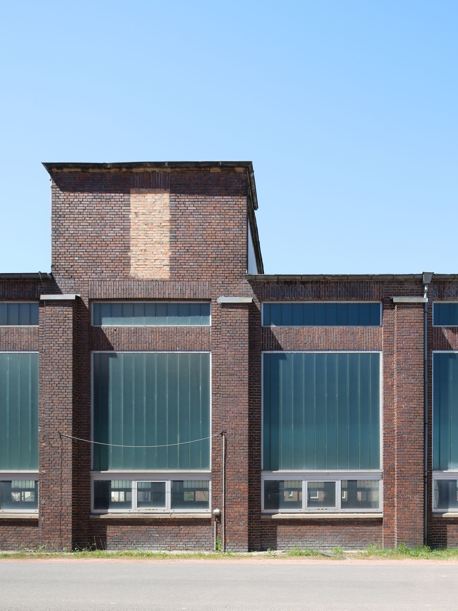 Dim industrial hall with weathered brick walls, large corrugated metal roller doors, and old control panels mounted on a pillar.